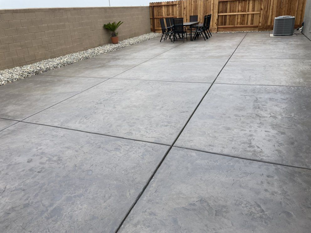 Empty concrete patio with outdoor table and chairs beside a fence and gravel border