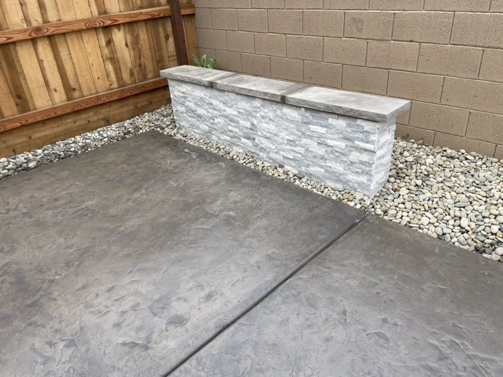 Concrete patio with a stone bench against a block wall and gravel border by a wooden fence.