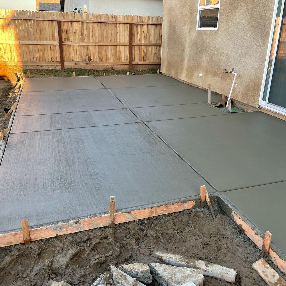 Freshly poured concrete patio slabs in a backyard beside a house and wooden fence.