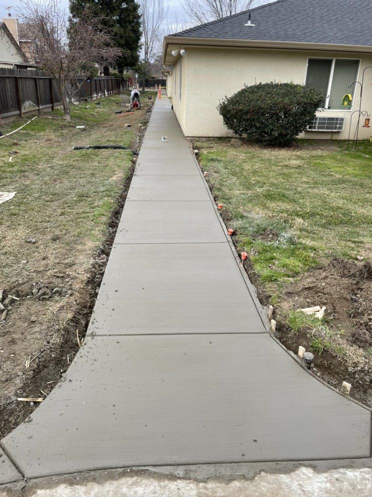 New concrete sidewalk leading to a beige house with a trimmed bush and yard.
