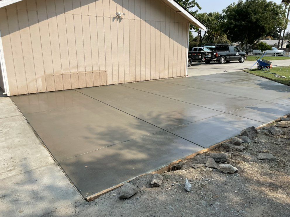 Concrete driveway beside beige garage, with a wet section and rocks along the edge.
