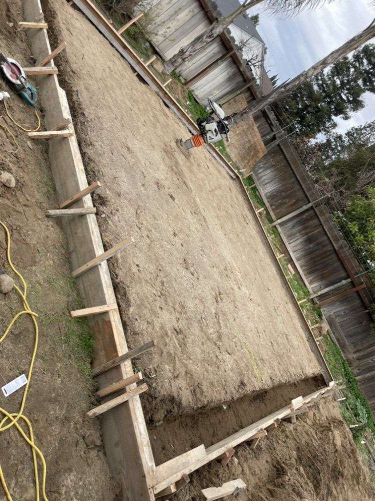 Wooden forms outline a rectangular foundation slab at a construction site with gravel and dirt.
