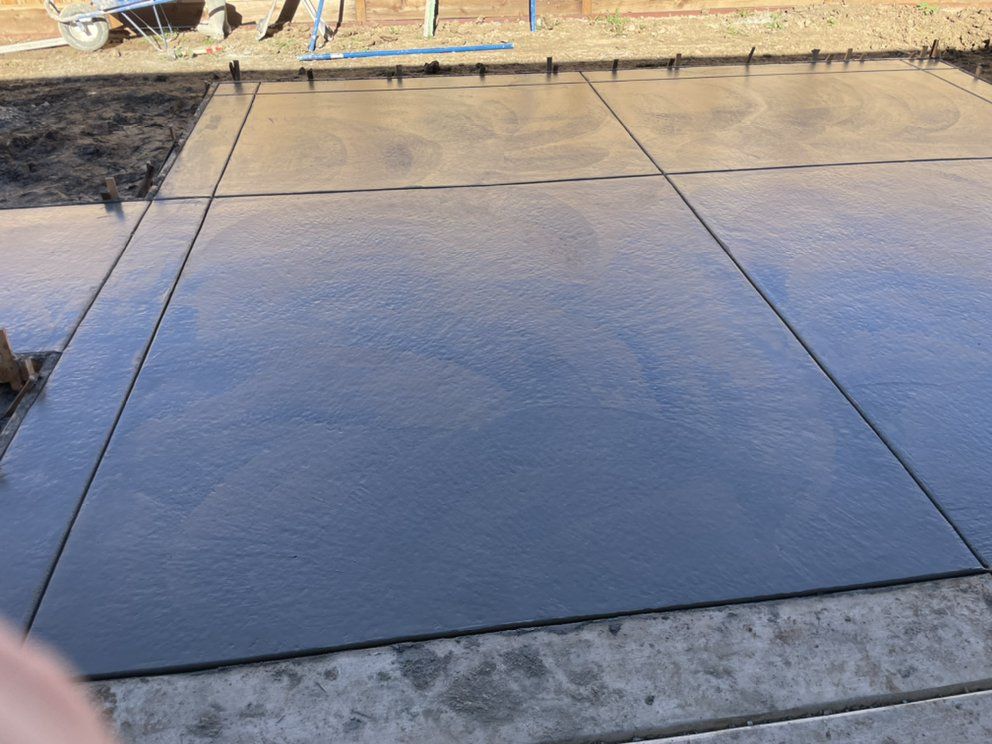 Freshly poured dark concrete driveway section with expansion joints and surrounding dirt edges