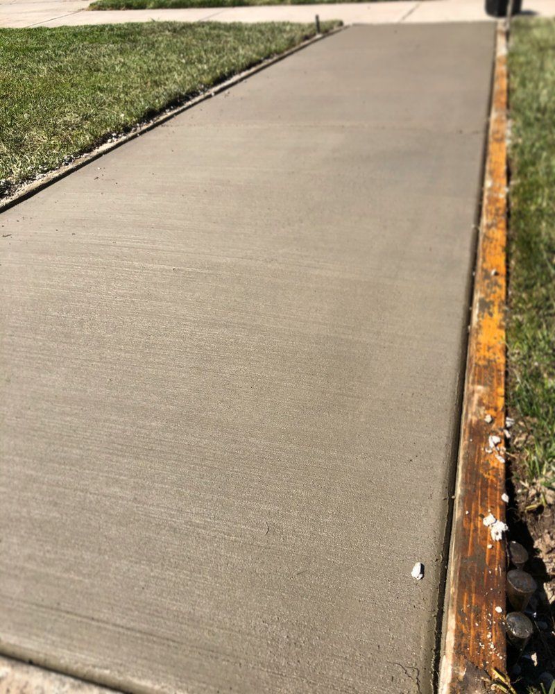 Freshly poured concrete sidewalk beside grass and a wooden form edge.