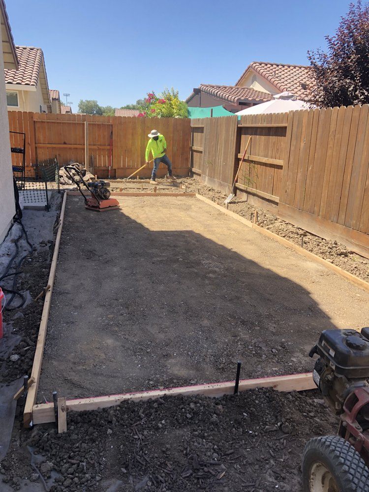 Construction worker grading dirt in a fenced backyard under a clear sky