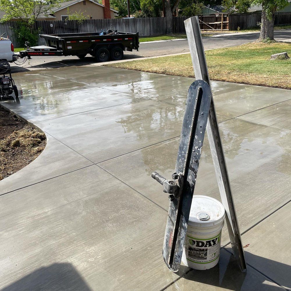 Wet concrete driveway with a squeegee leaning against a white bucket in the foreground