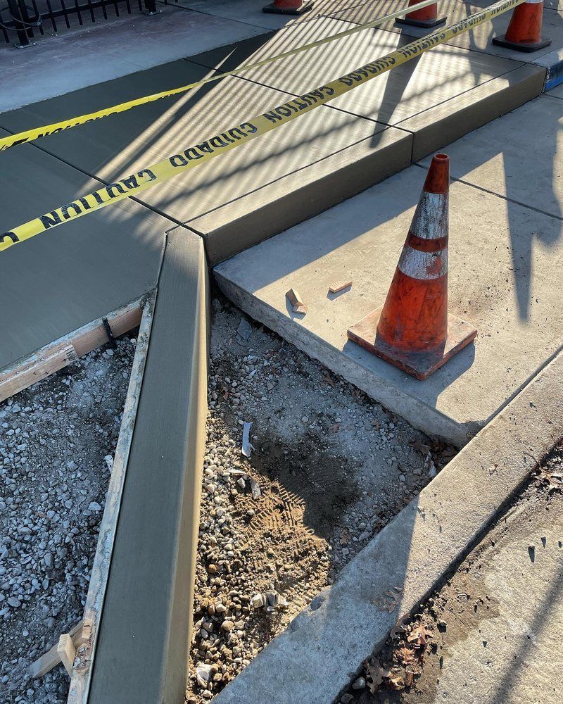 Orange cone and caution tape marking a broken sidewalk around an exposed hole.