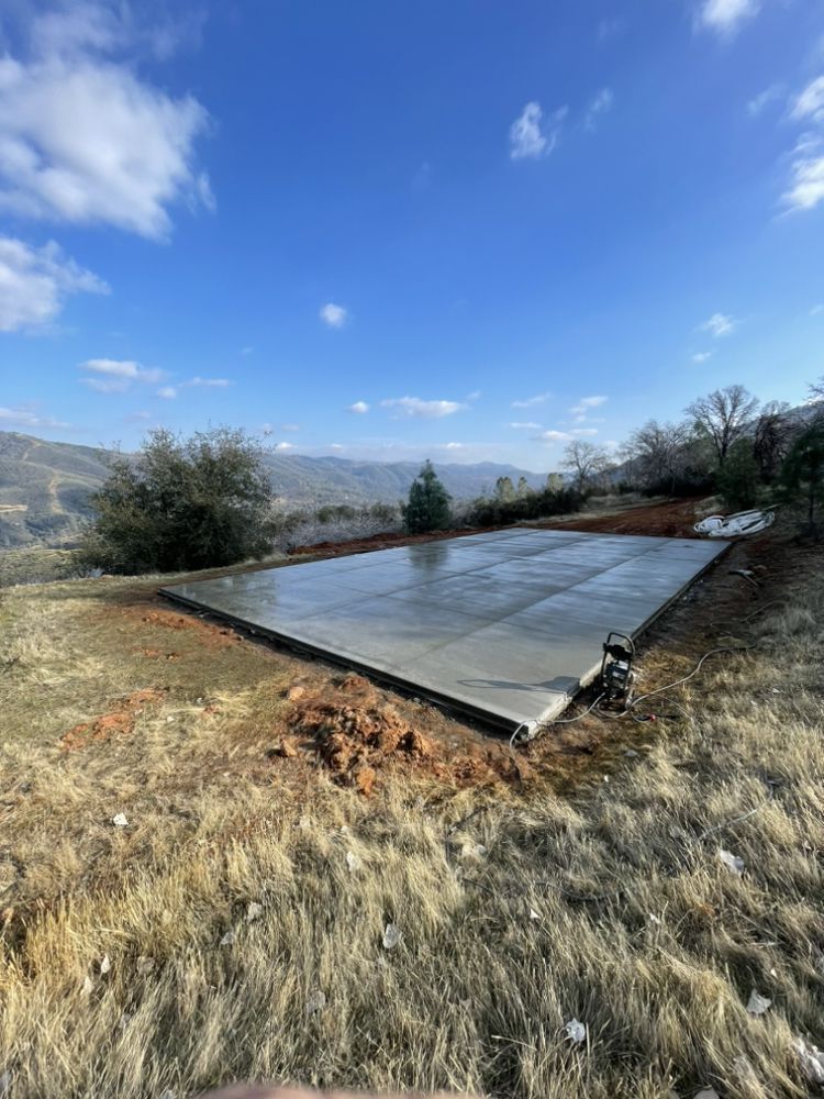 Rectangular concrete foundation on a grassy hillside under a blue sky with clouds