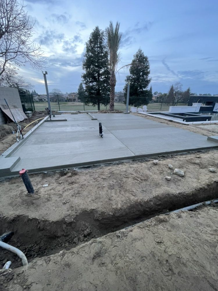 New concrete slab foundation at a construction site, with trenches, pipes, and trees in the background