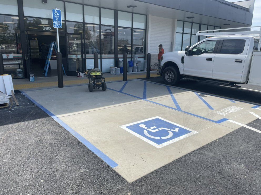 Accessible parking spaces with blue markings outside a storefront entrance; a pickup truck is parked nearby.