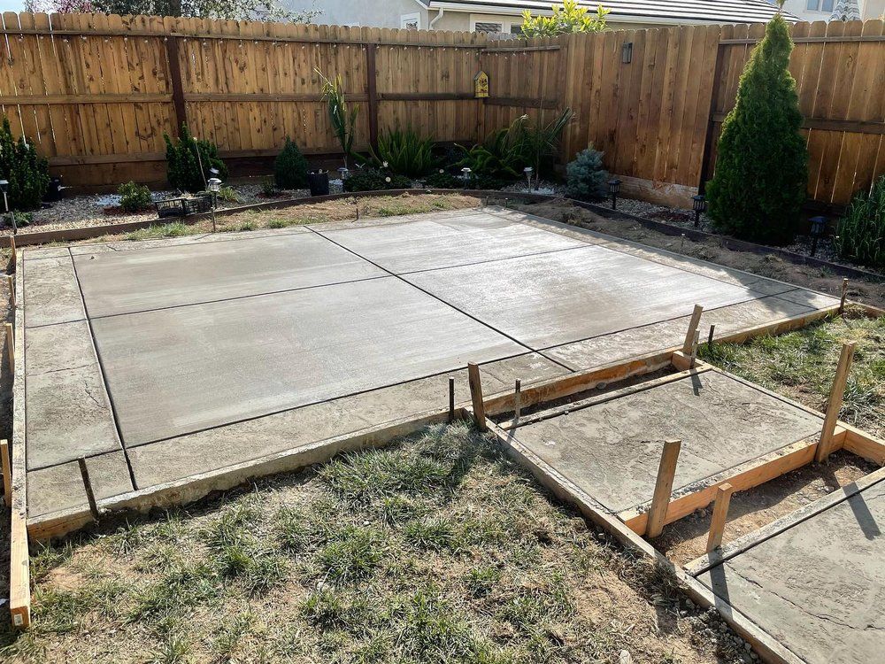 Backyard concrete patio under construction with wooden forms and a fenced perimeter