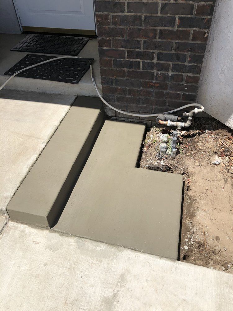 Concrete step and walkway repair beside a brick wall, with exposed dirt and plumbing pipes.