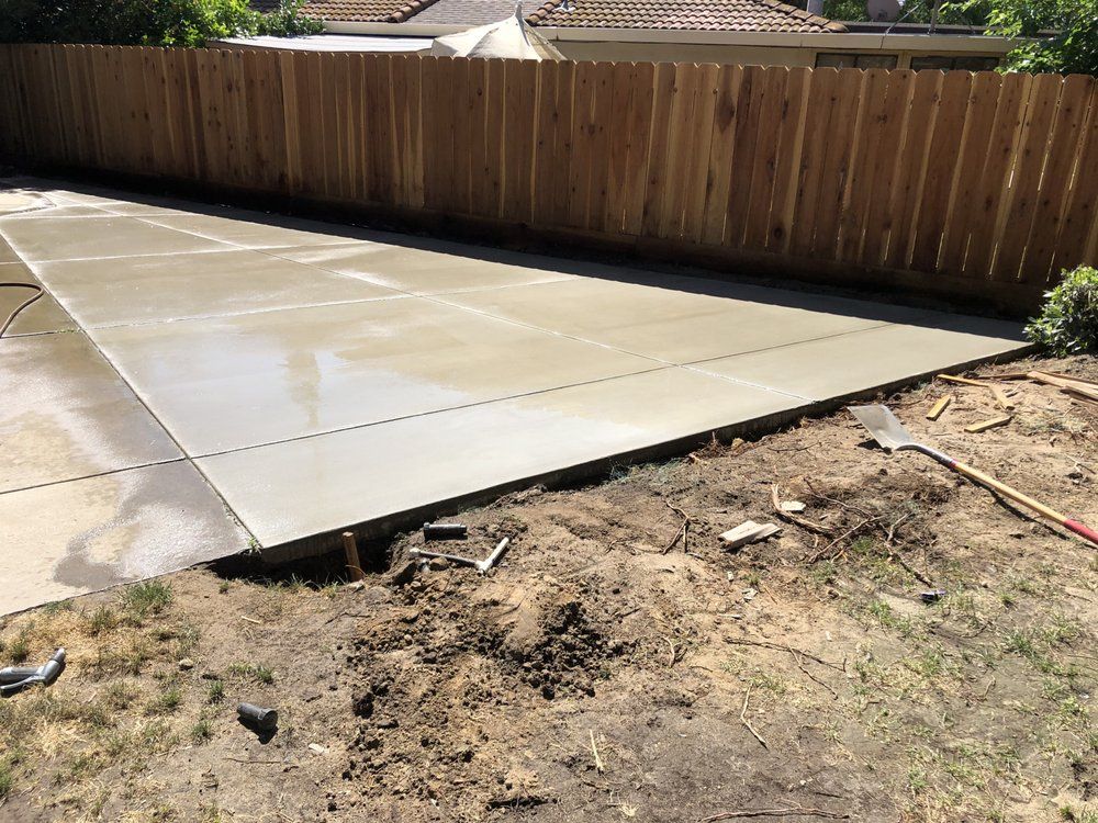 Concrete driveway beside a wooden fence, with a patch of bare dirt in the foreground