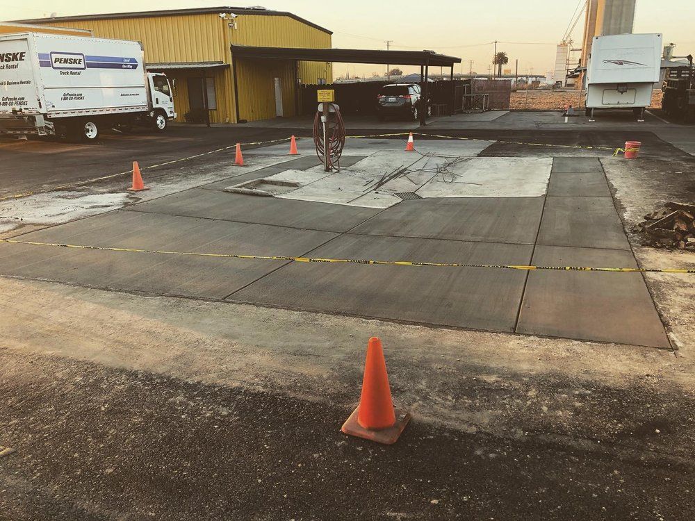Industrial yard with traffic cones around a damaged concrete pavement area at sunset.