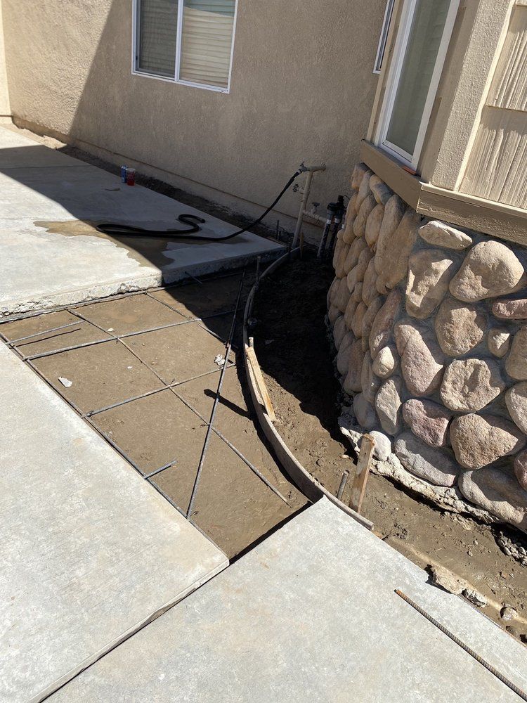 Damaged walkway and exposed black cable beside a tan house with stone foundation.