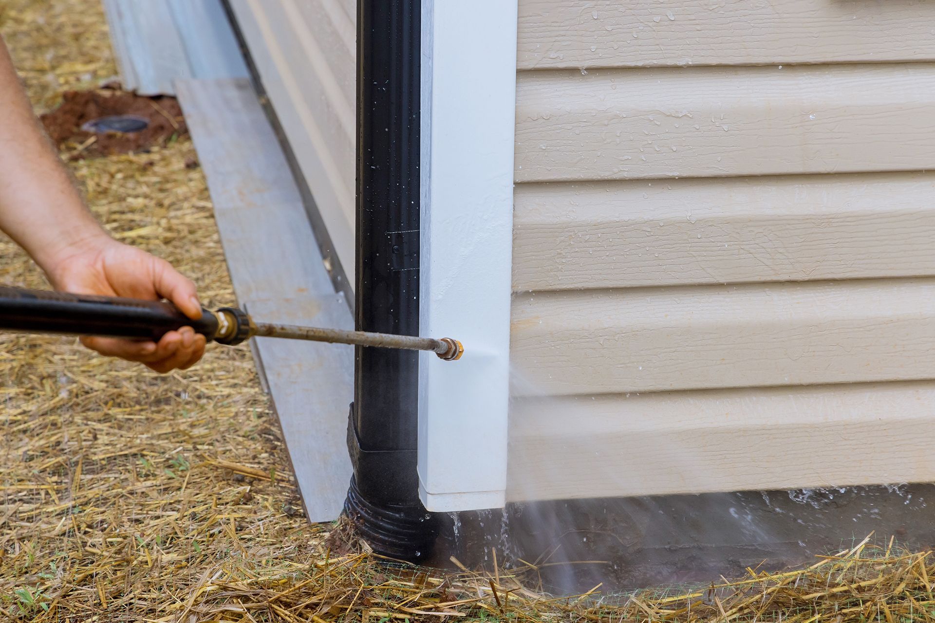 A person is cleaning the side of a house with a pressure washer.