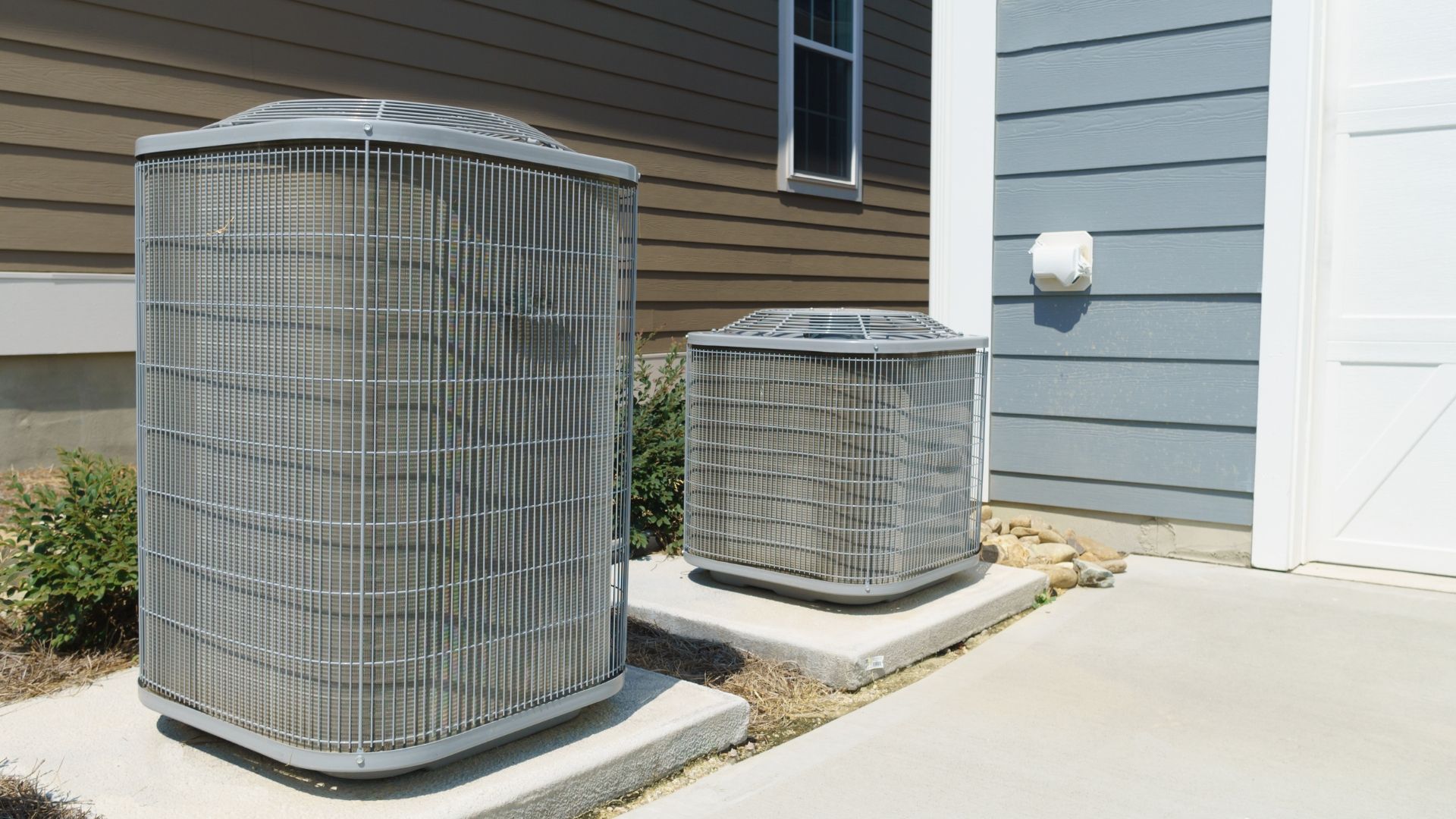 Two outdoor air conditioning units beside a house on a concrete pad