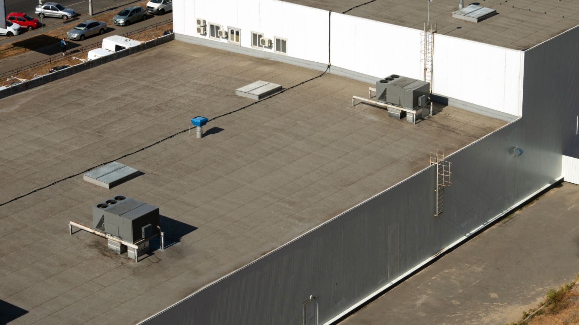 Aerial view of a flat white rooftop with HVAC units and vents on an industrial building.