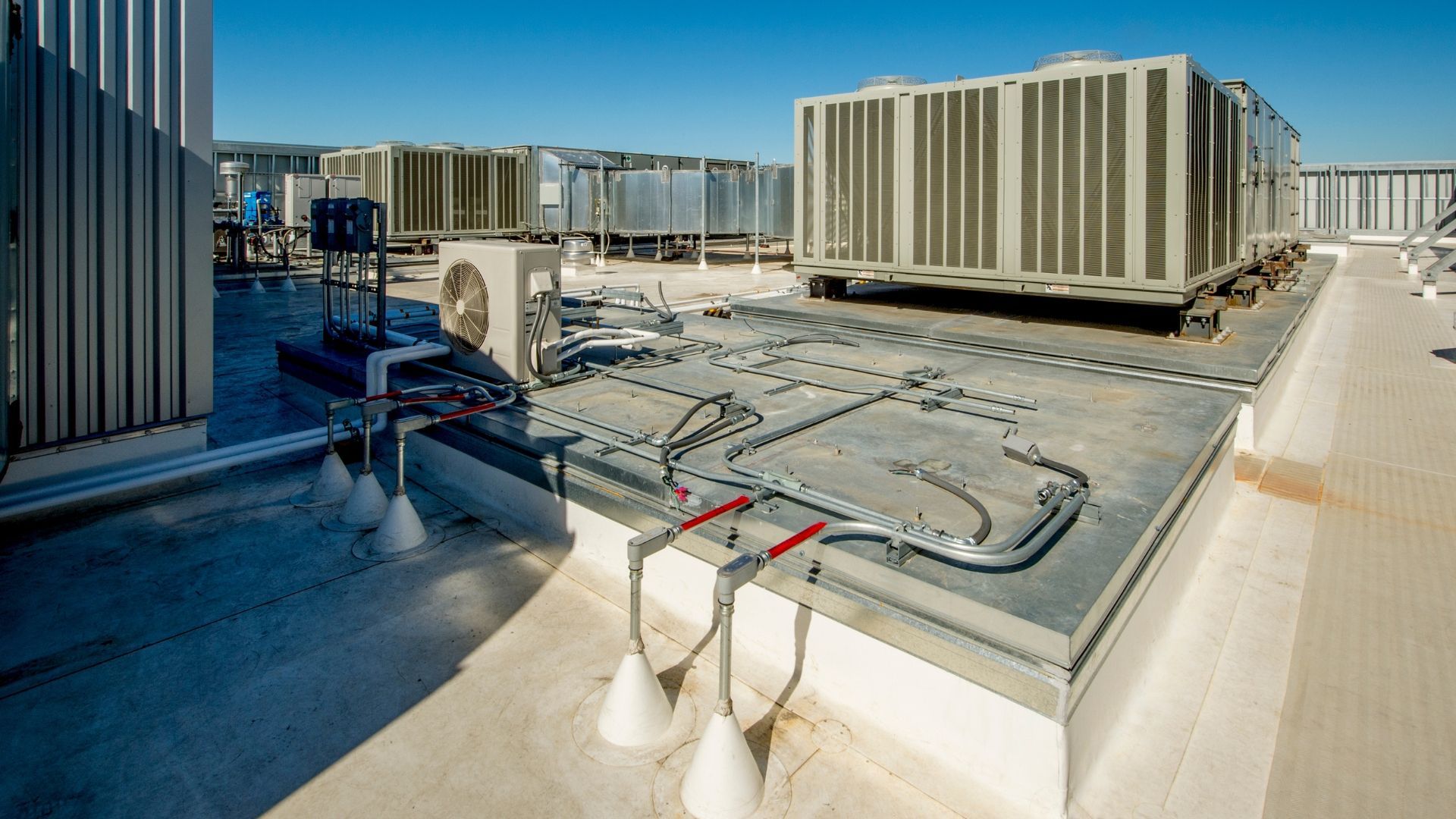 Rooftop HVAC units and piping on a sunlit building rooftop with city skyline in the background