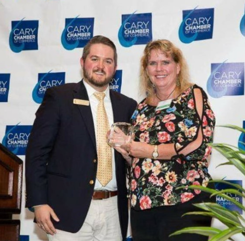A man and woman are posing for a picture in front of a cary chamber backdrop