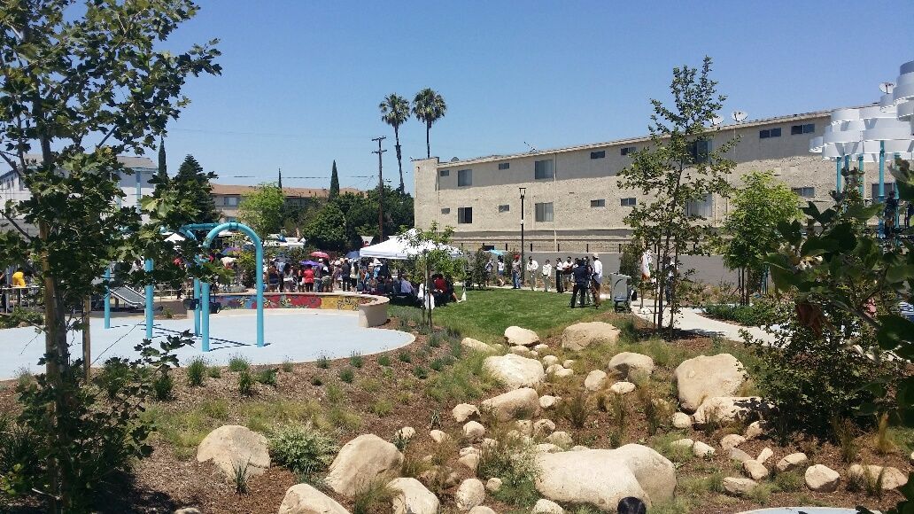 Park scene with a water play area, a grassy hill, and people near a building. Sunny day.