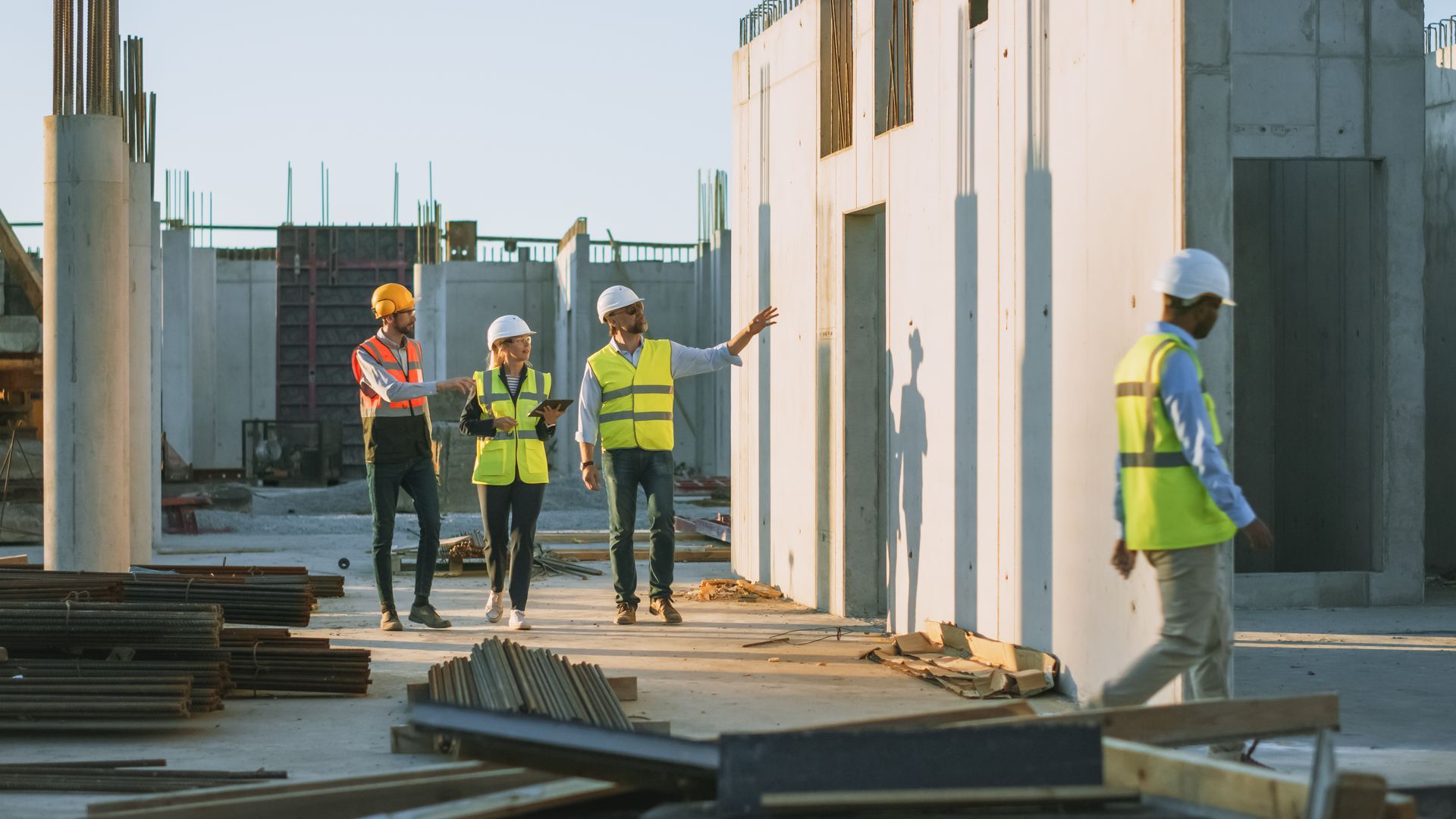 Construction contractors wearing safety vests inspect a concrete building site together.