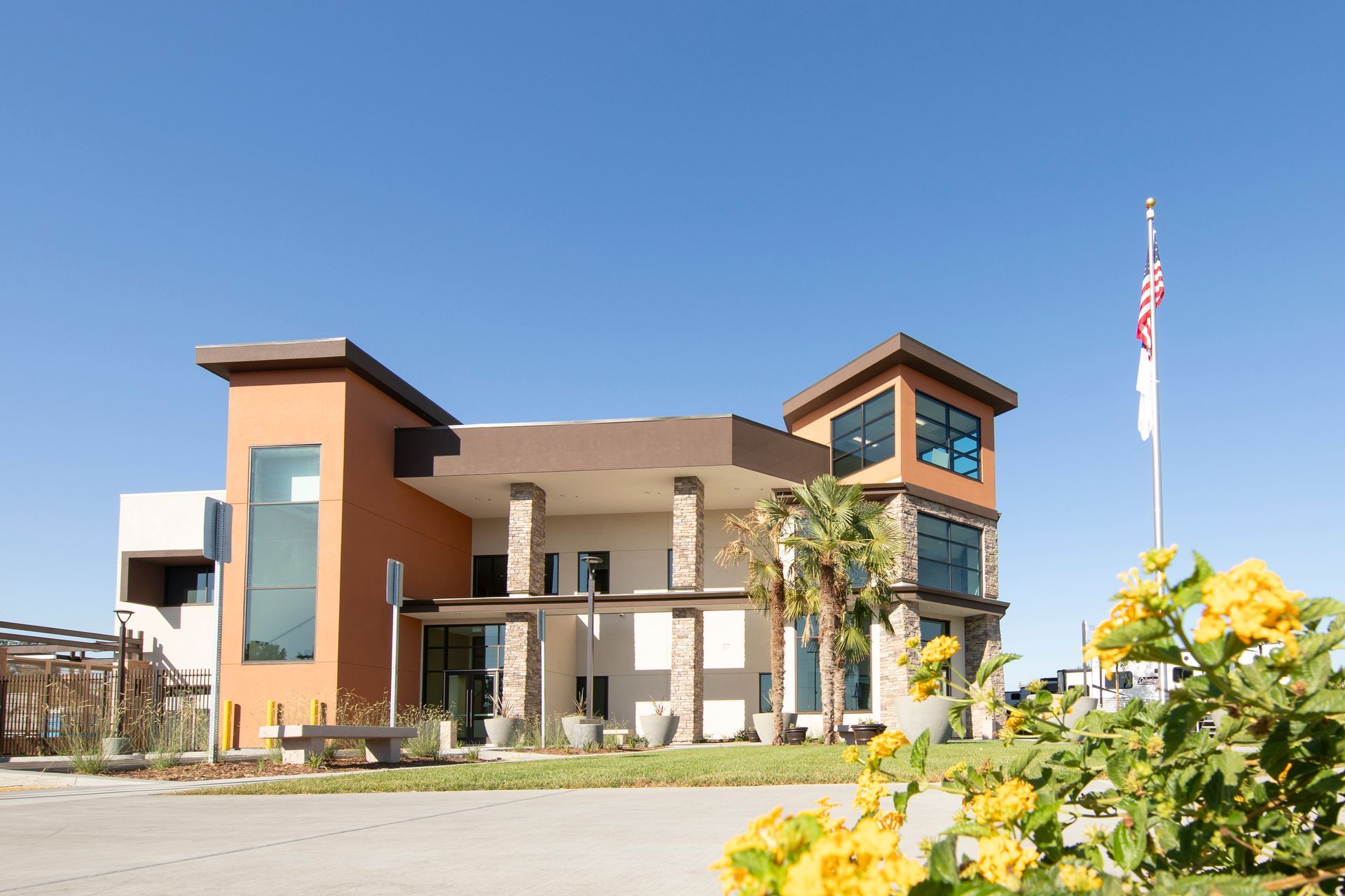 Modern building with orange and tan exterior, American flag, and yellow flowers in foreground.