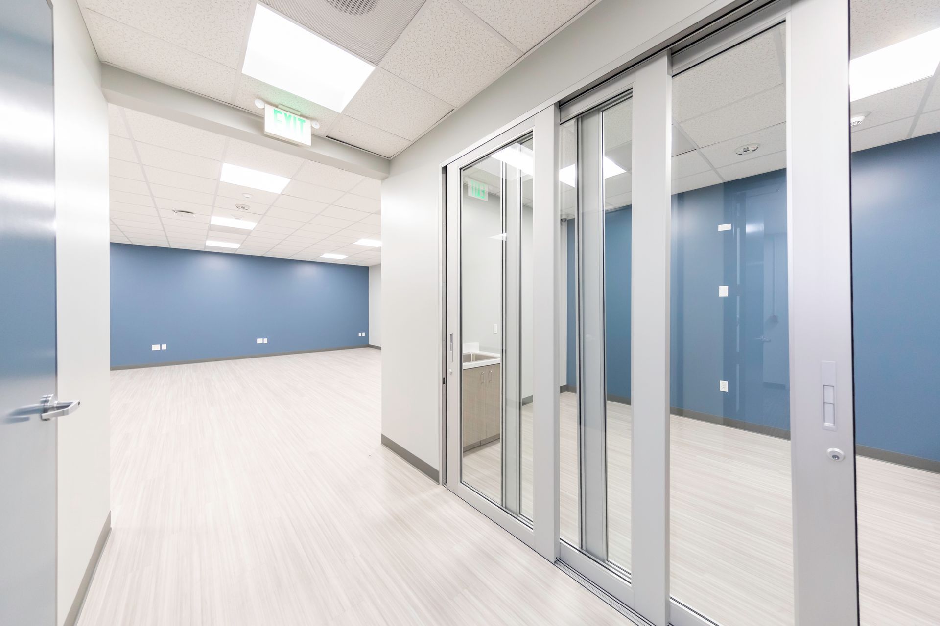 Empty office hallway with glass doors, light blue walls, and white floors.
