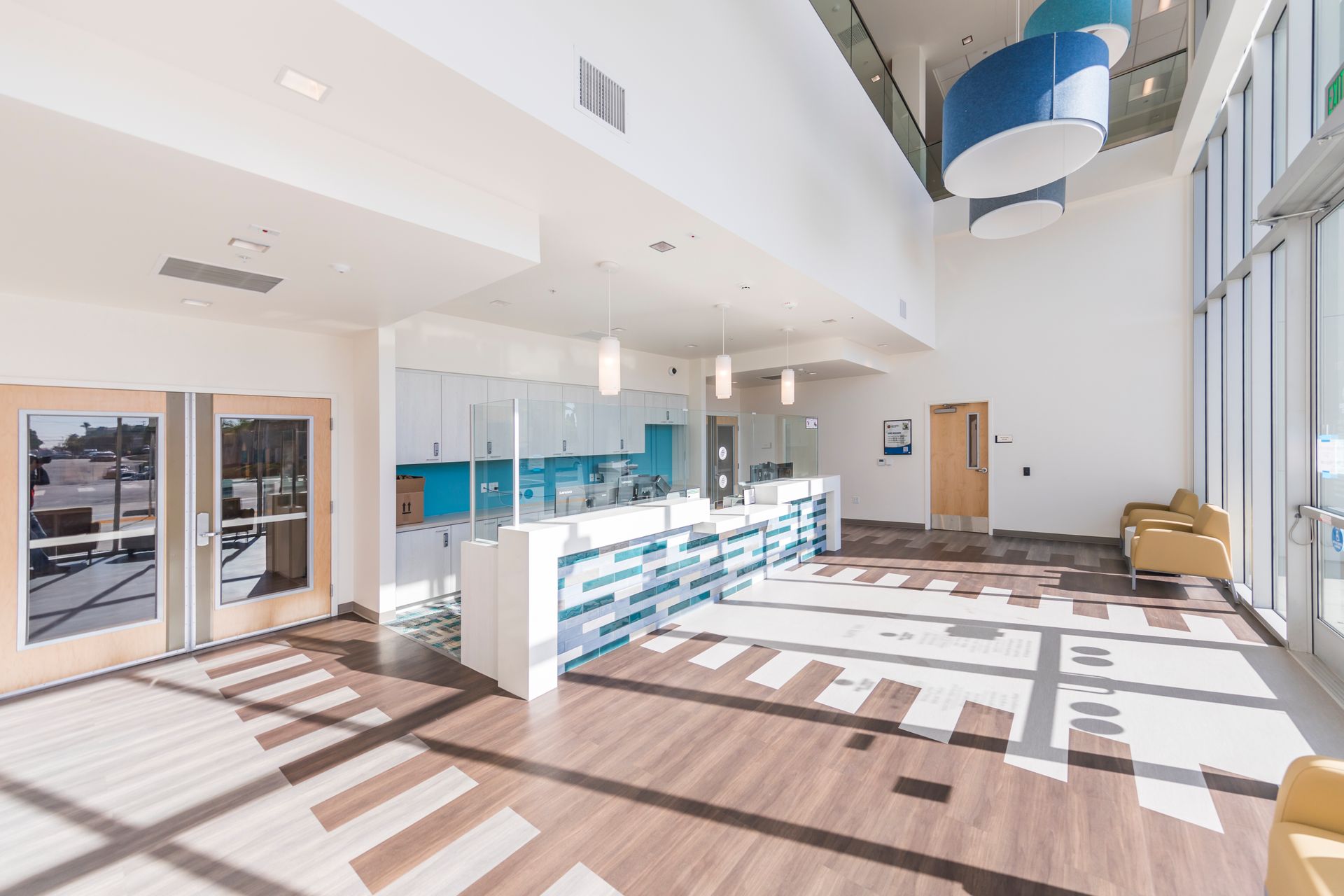 A modern, bright medical or professional reception area with a blue desk, wood-patterned floors, and high ceilings.