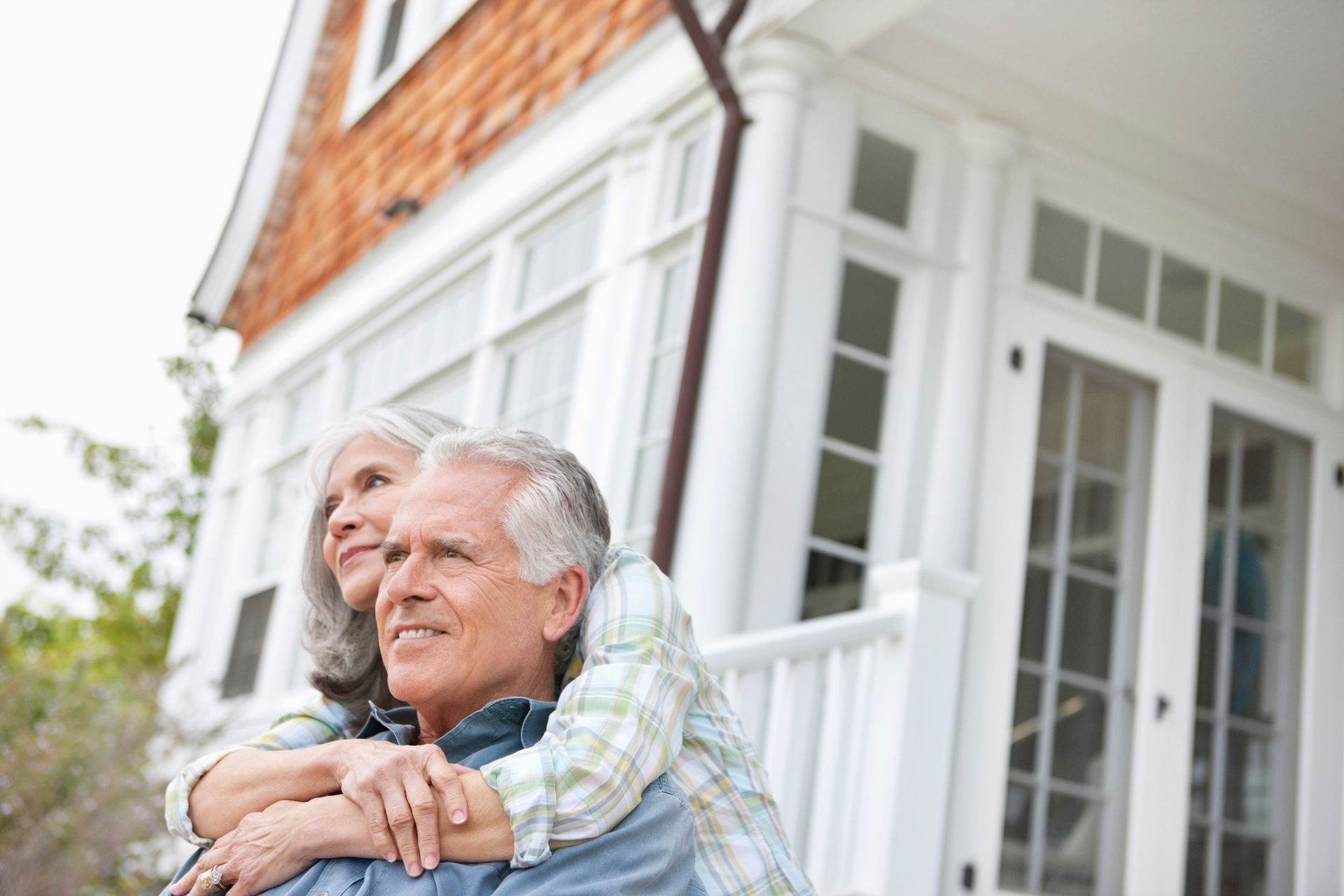 A senior couple hugs while sitting outside, in front of a blurry house.