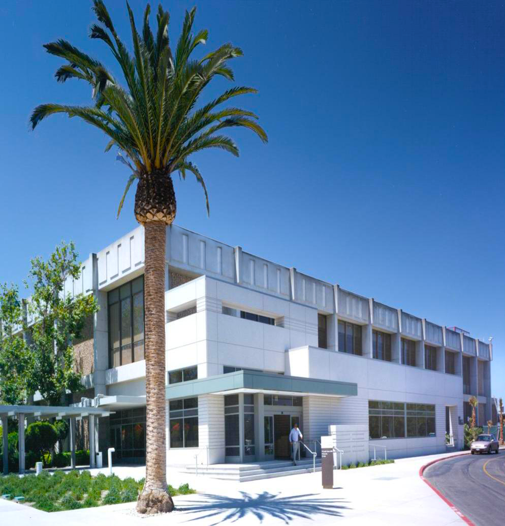 Modern white building with palm tree; person at entrance under blue sky.