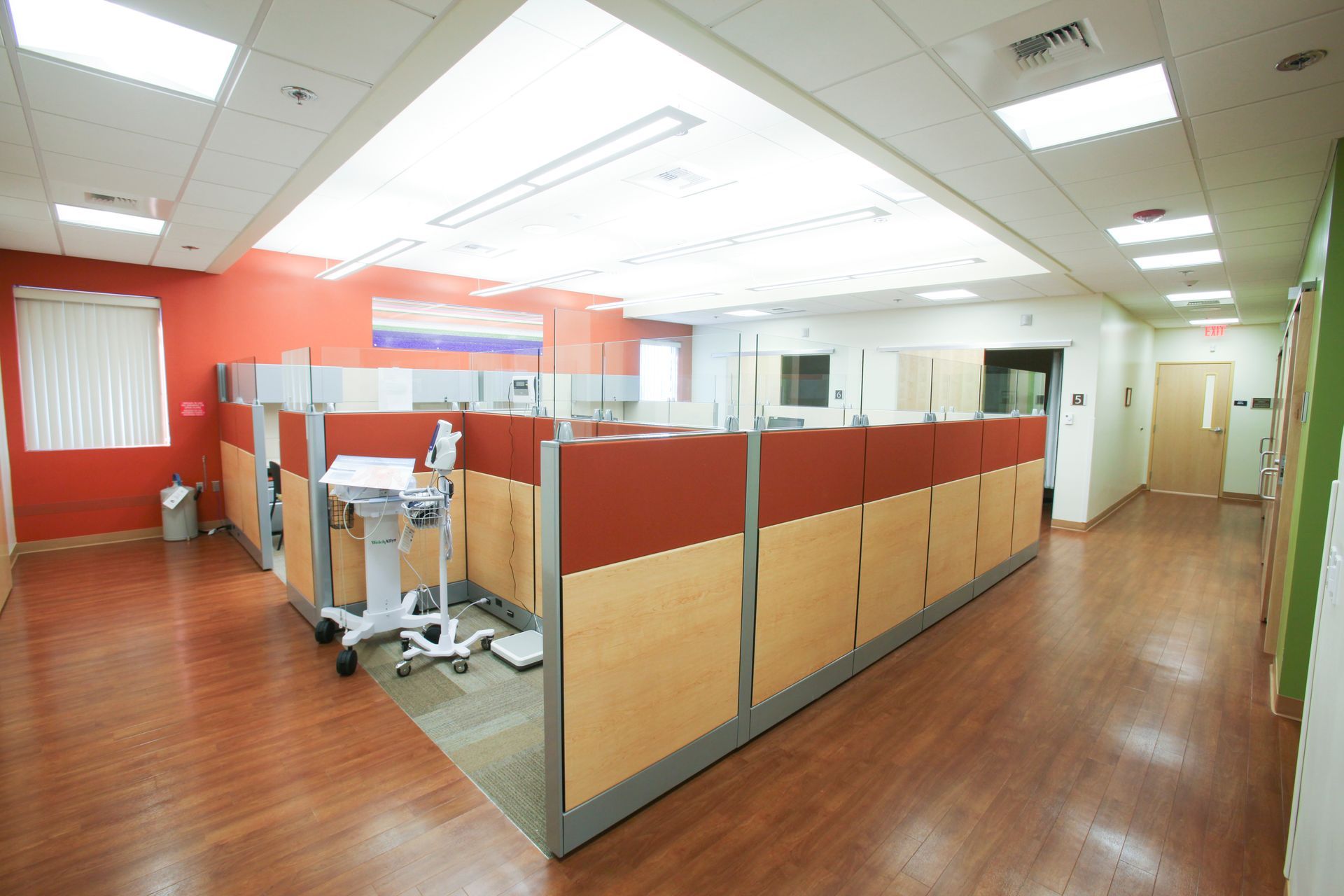 Office cubicles with red and beige panels, wood flooring, and overhead lighting.