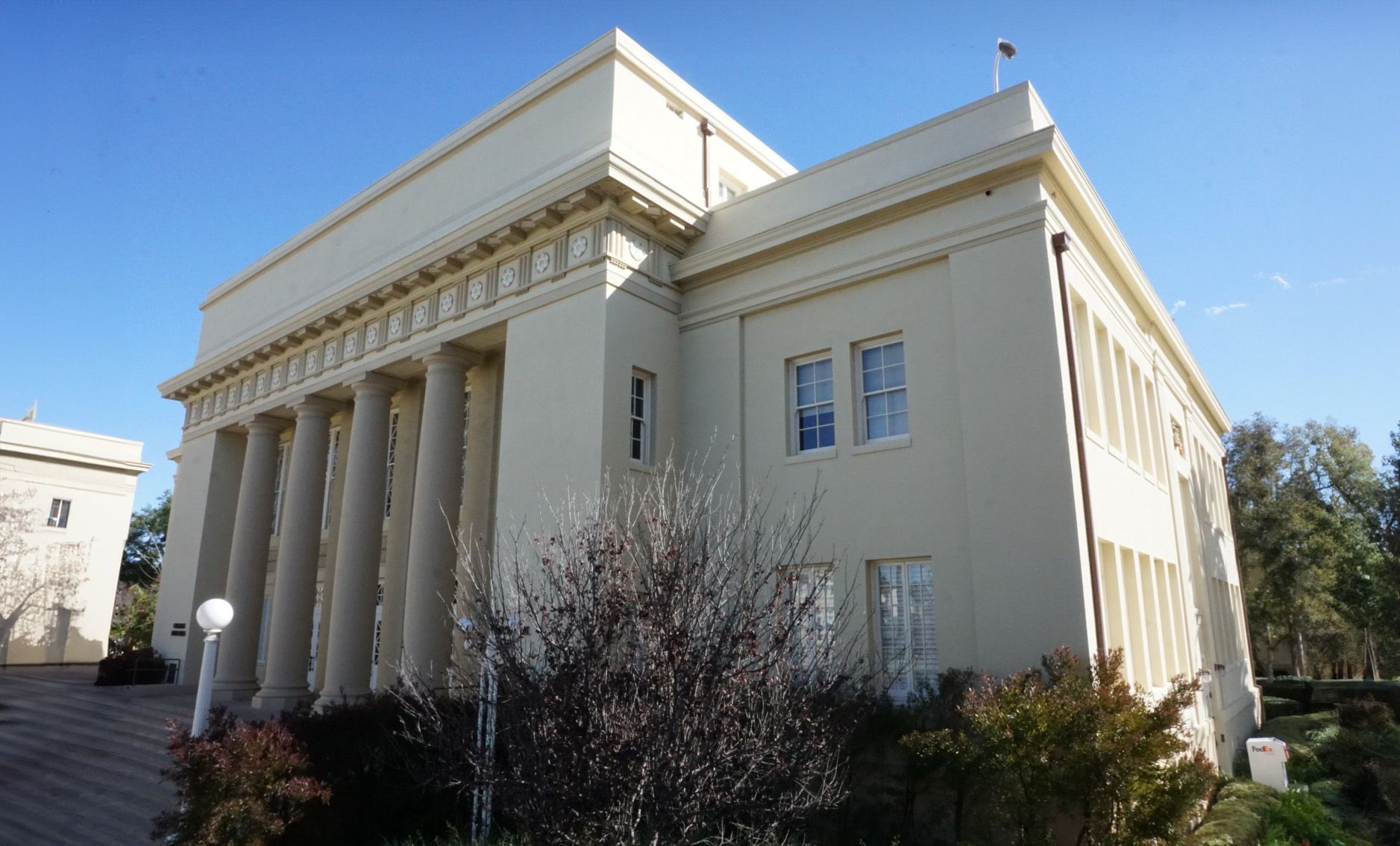 A light-colored, neoclassical building with a row of columns at the entrance under a clear blue sky.