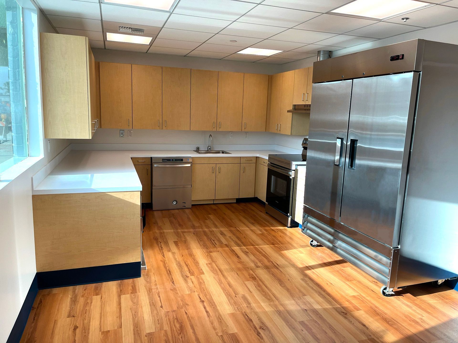 Kitchen with wood floor and cabinets, white countertops, stainless steel appliances, and a window.