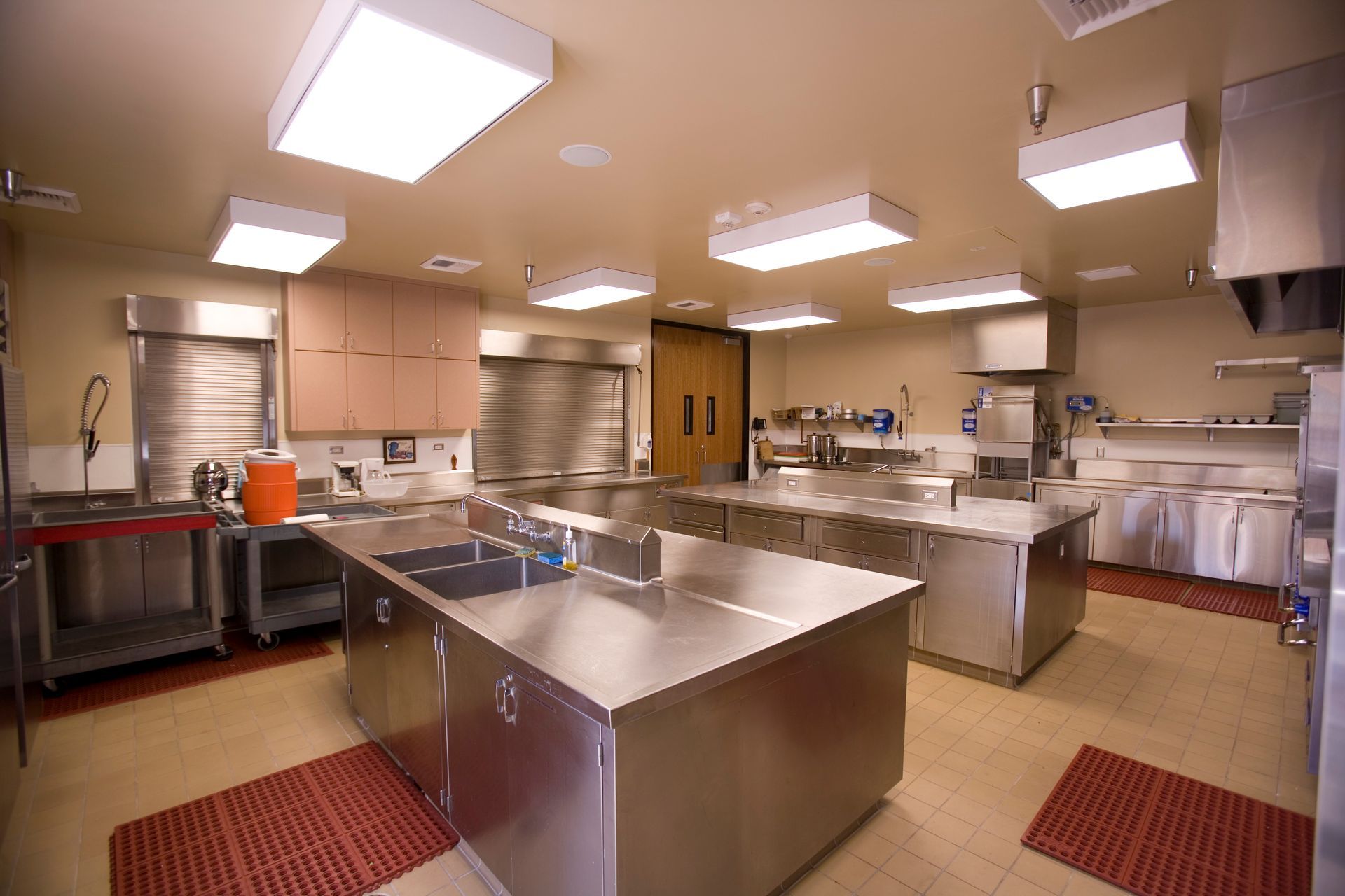 Commercial kitchen with stainless steel counters, sinks, and appliances; overhead lighting.