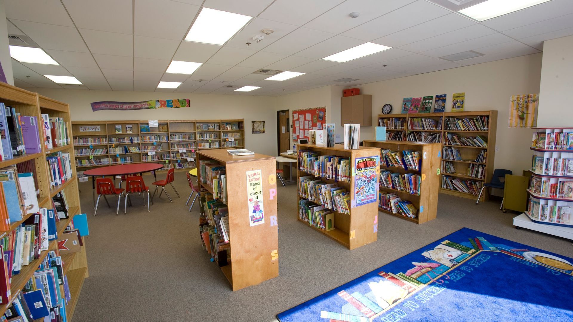 Library interior with bookshelves, tables, chairs, and colorful rugs.