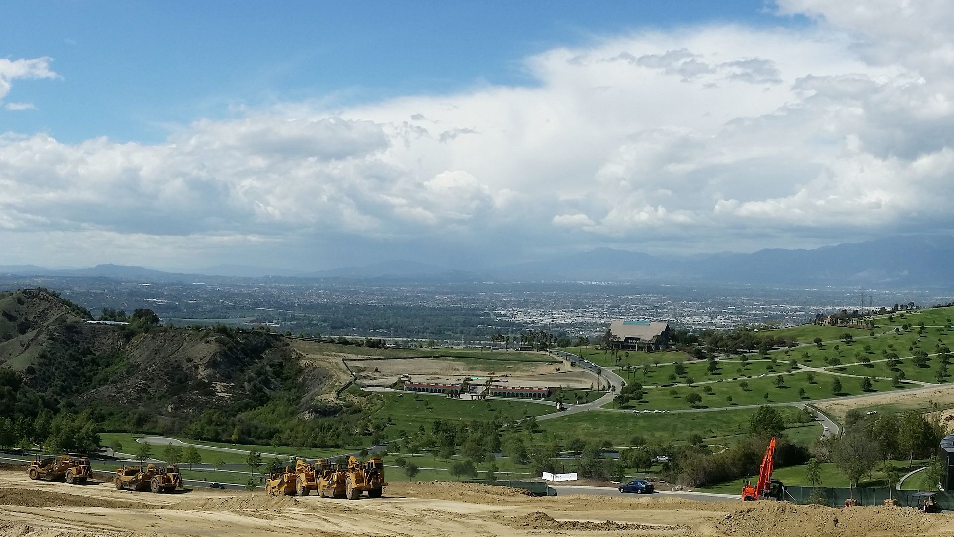 Construction site overlooking a city with cloudy sky. Yellow construction equipment.