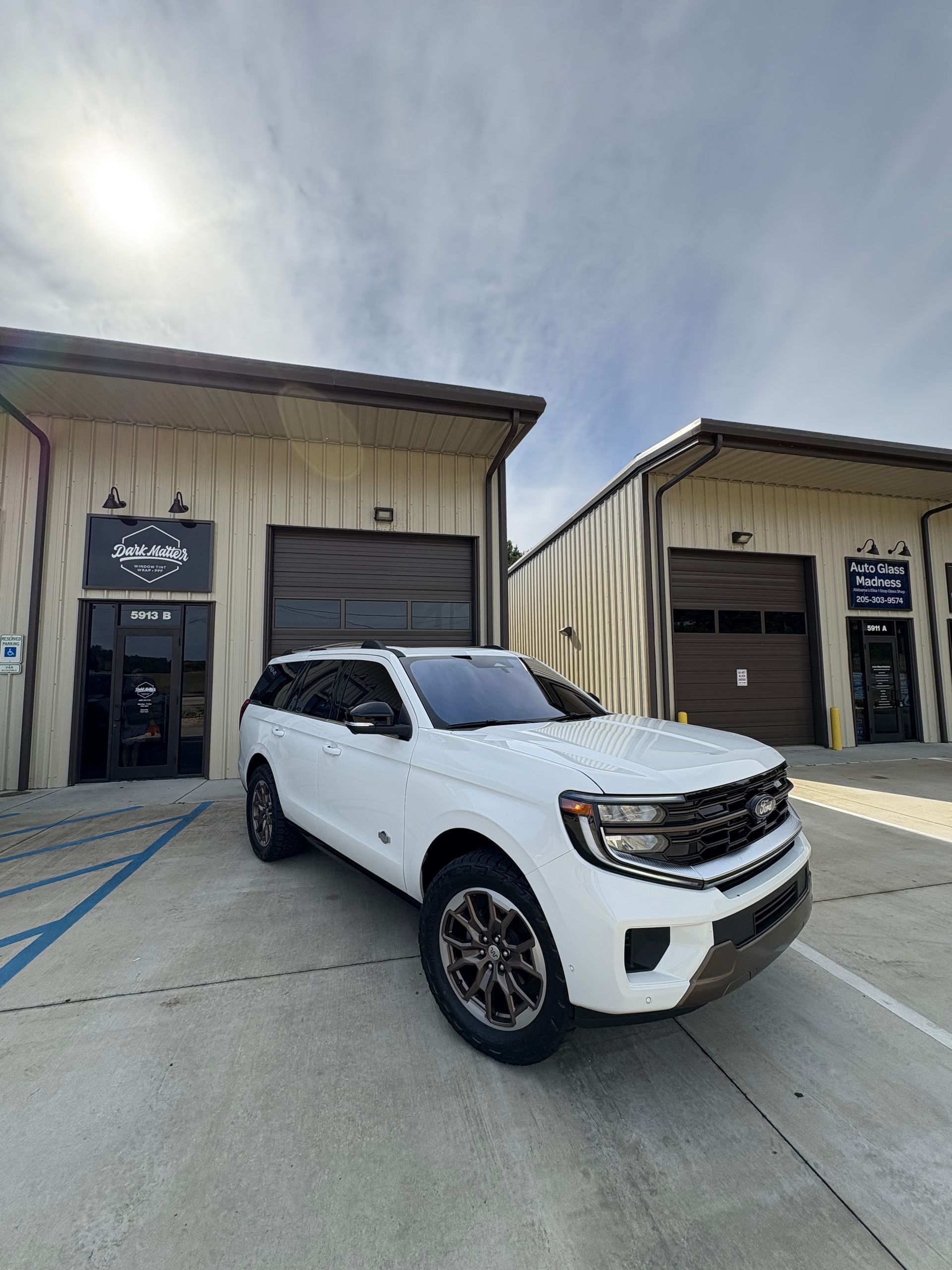 White Ford SUV parked in front of a tan building with closed garage doors. Sunny day.