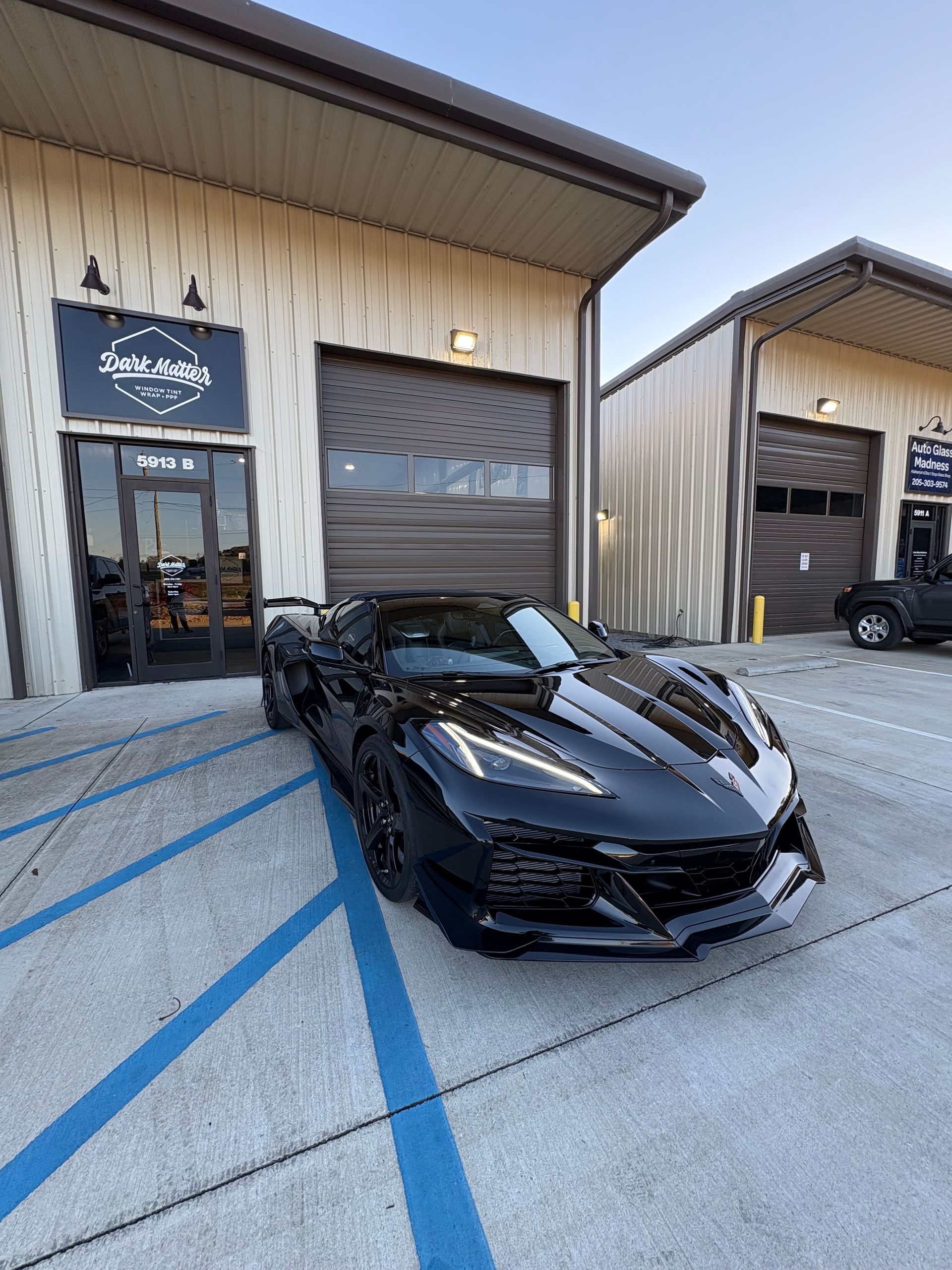 Black sports car parked in front of a building with a roll-up door; blue parking lines.