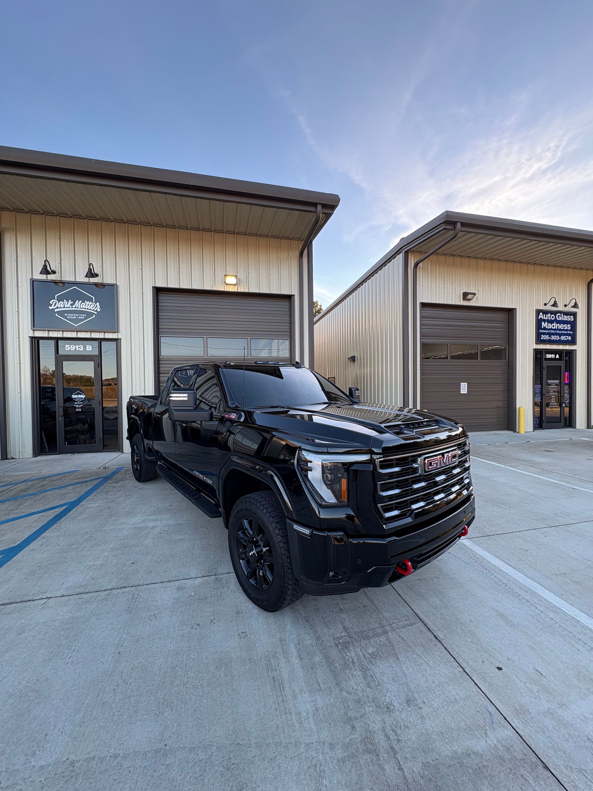 Black GMC truck parked in front of two garage-like buildings under a blue sky.
