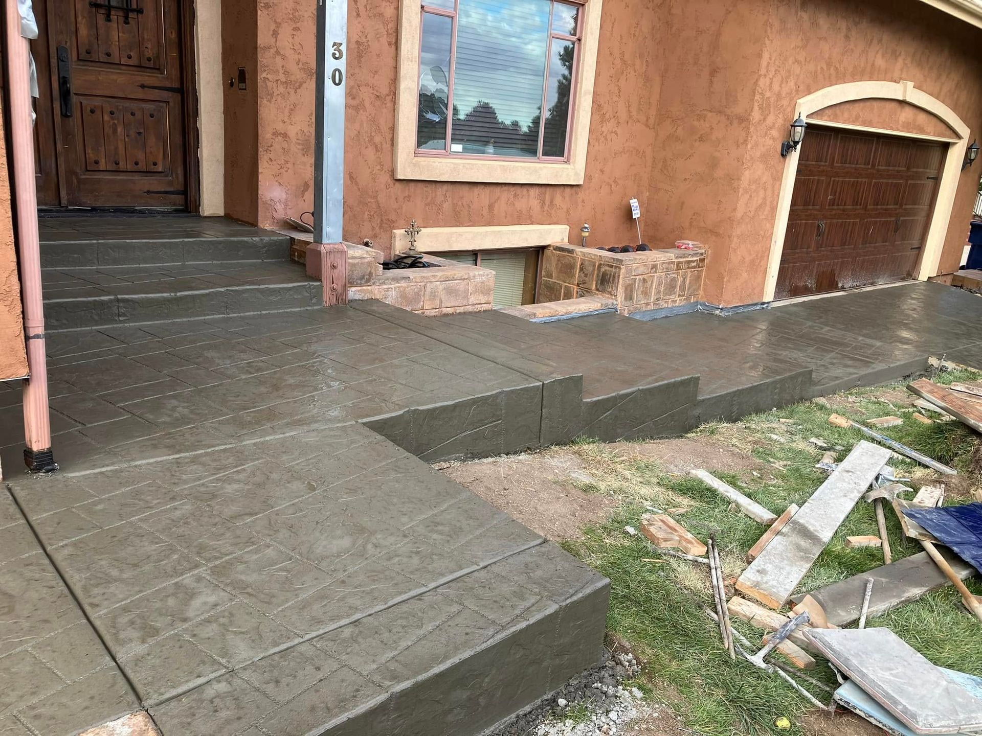Front porch with newly tiled ramp and steps leading to a wooden front door, beside a garage and yard debris