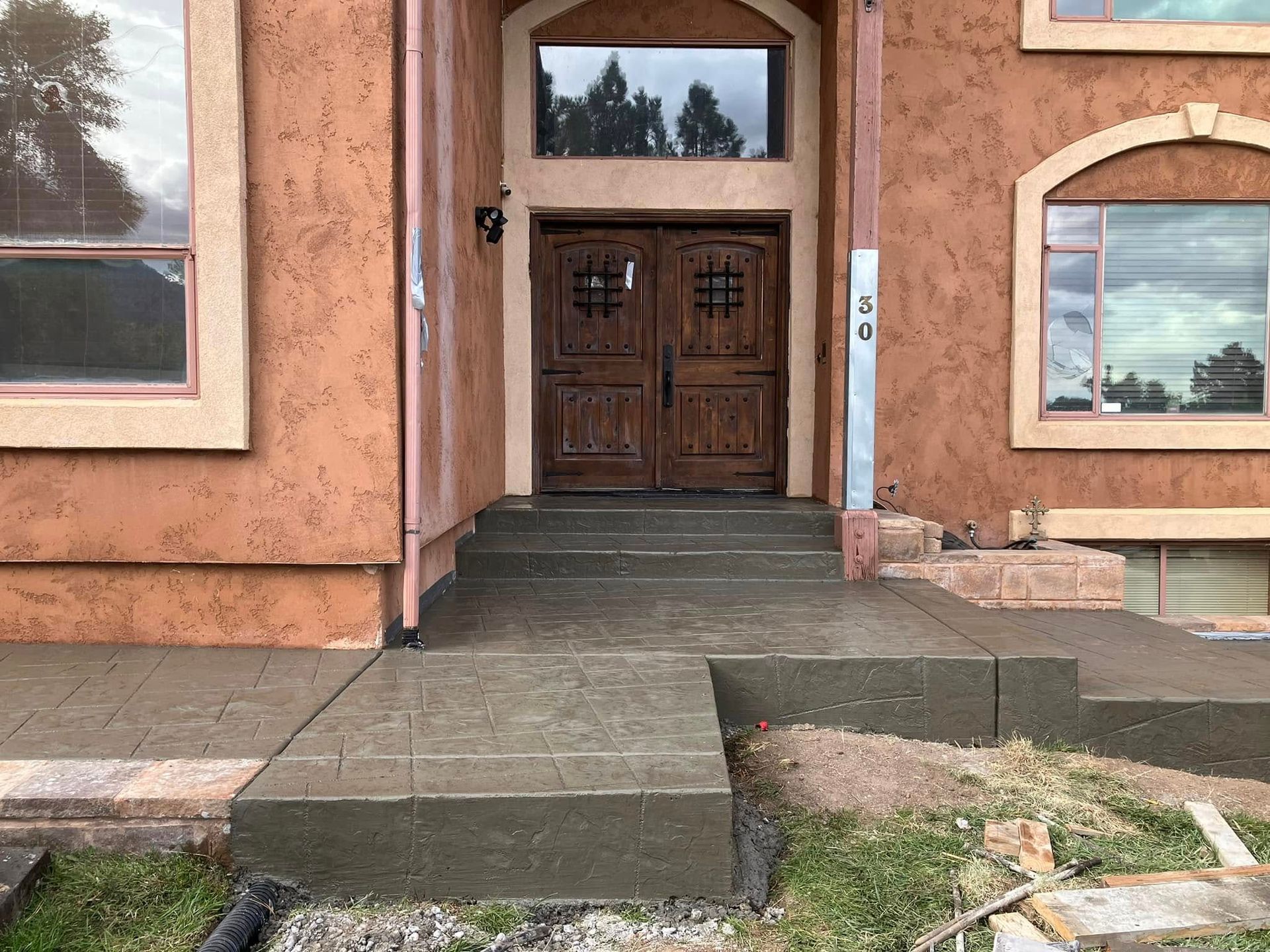 Front entrance of a stucco building with wooden double doors and a concrete ramp leading up to it