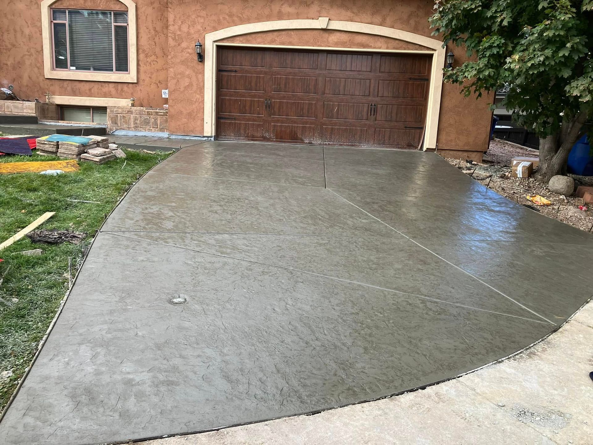 Freshly poured concrete driveway leading to a brick garage with a brown door