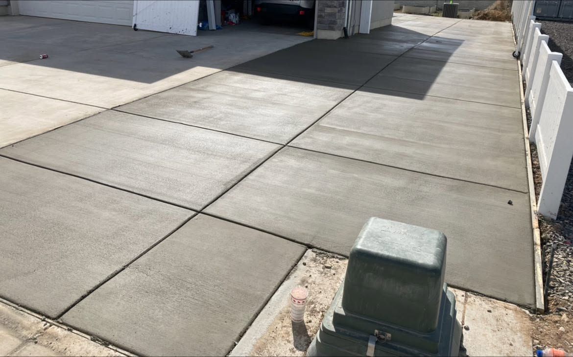 Concrete driveway leading to an open garage, with a green utility box in the foreground.