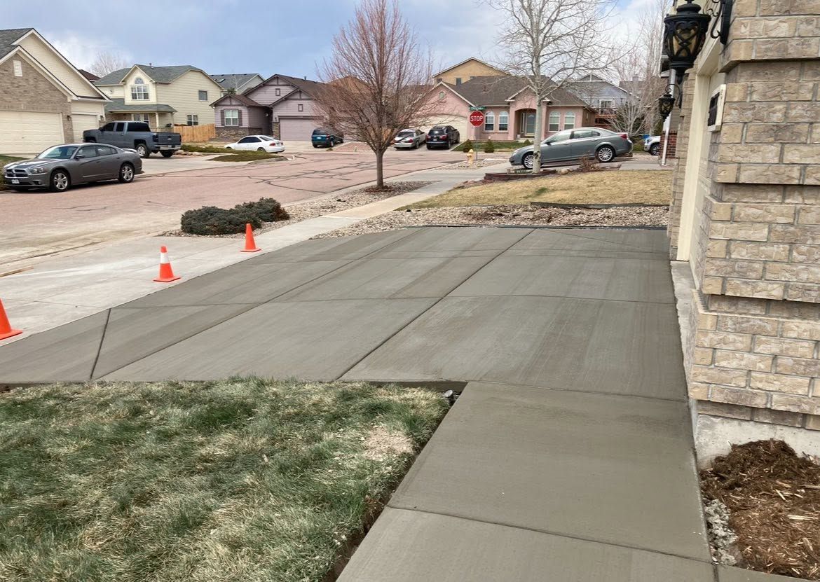 Freshly poured concrete sidewalk ramp at a suburban street corner with orange cones nearby