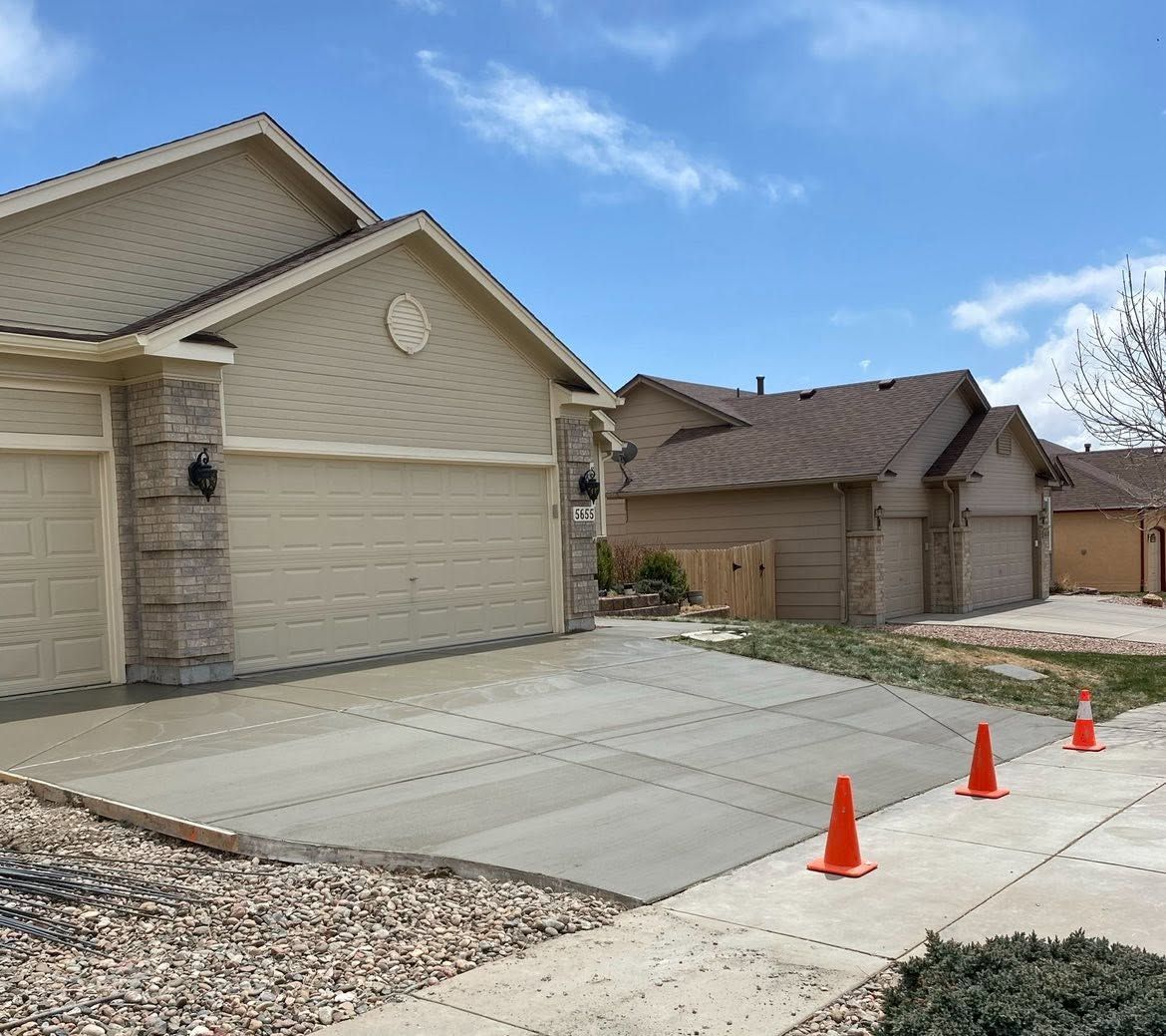 Suburban house driveway with three orange cones near the sidewalk under a blue sky