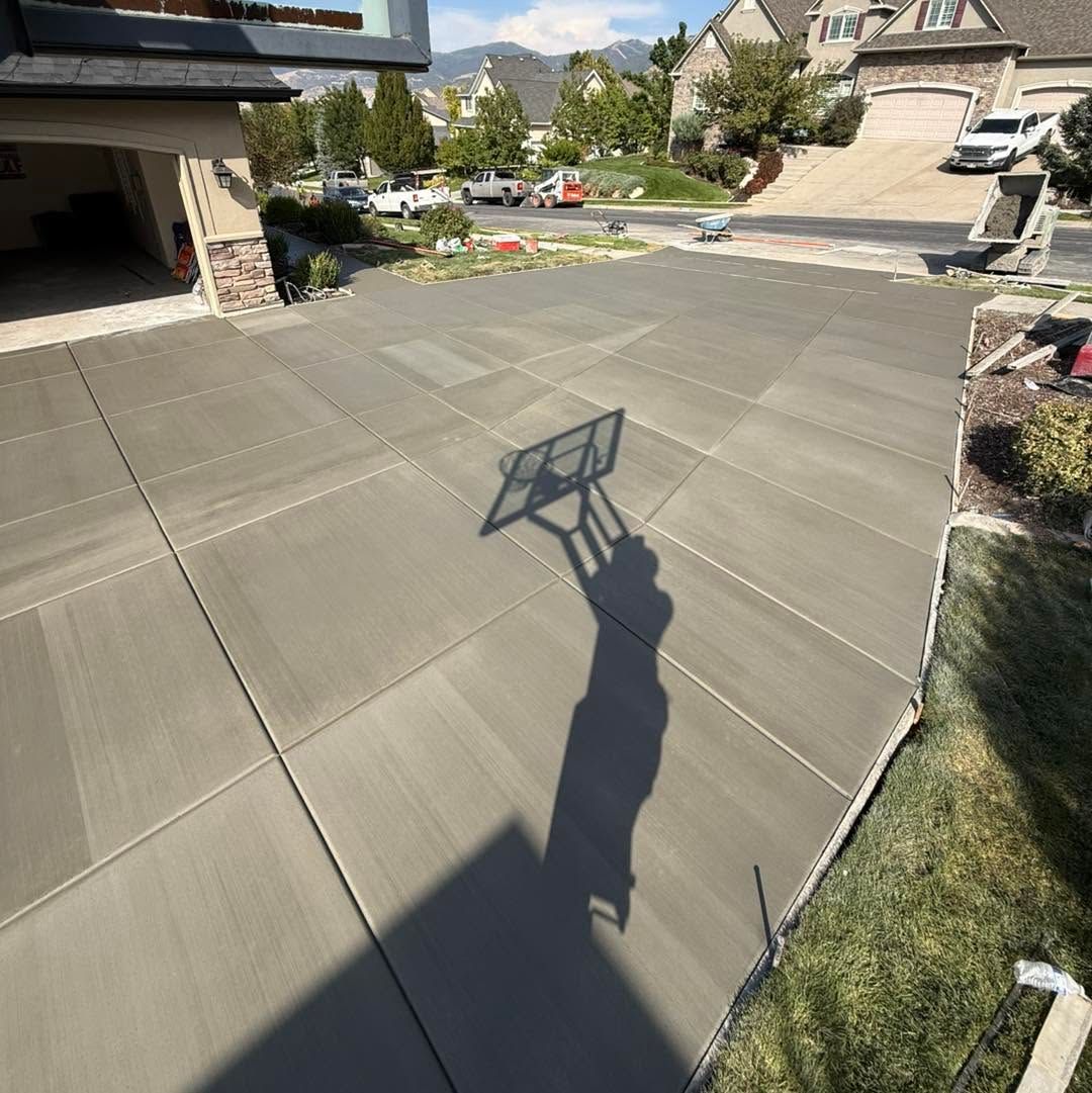 Sunlit concrete driveway and patio with mountain homes in the background and a basketball hoop shadow in the foreground