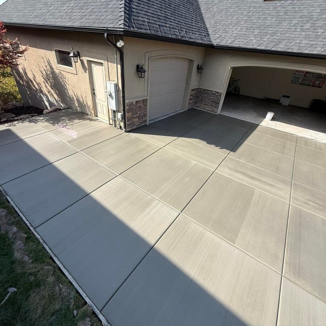 Concrete driveway and covered garage area beside a tan house with a tiled roof.