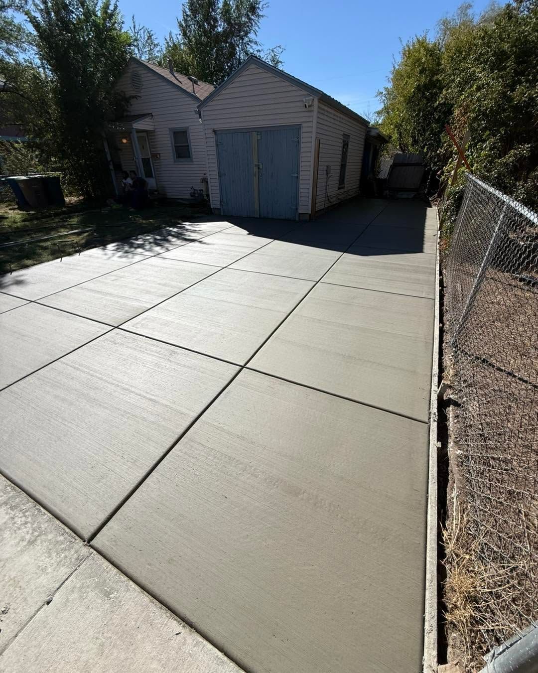Concrete driveway leading to a small garage beside a chain-link fence on a sunny day