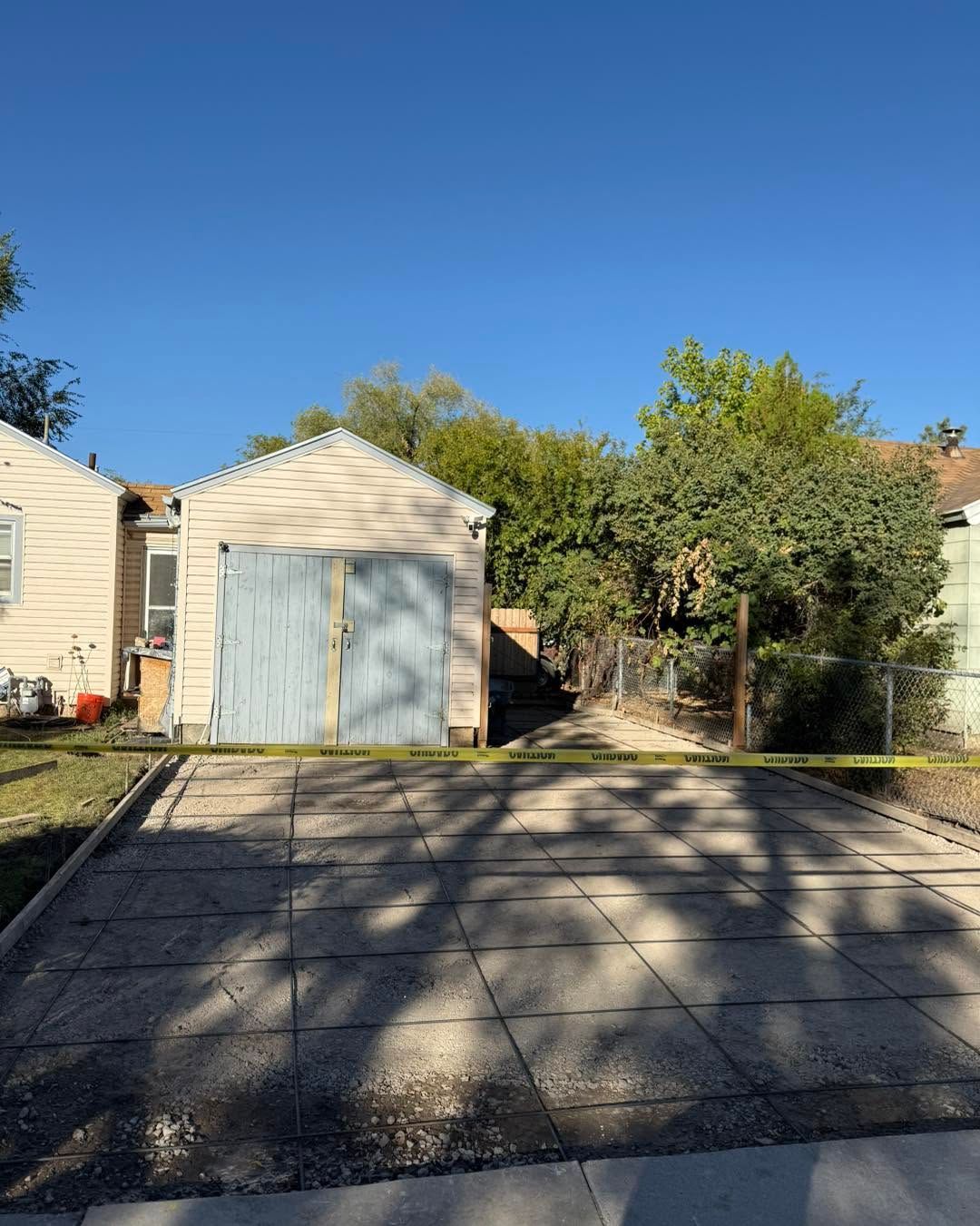 Driveway leading to a small white garage, with trees and neighboring houses under a clear blue sky.
